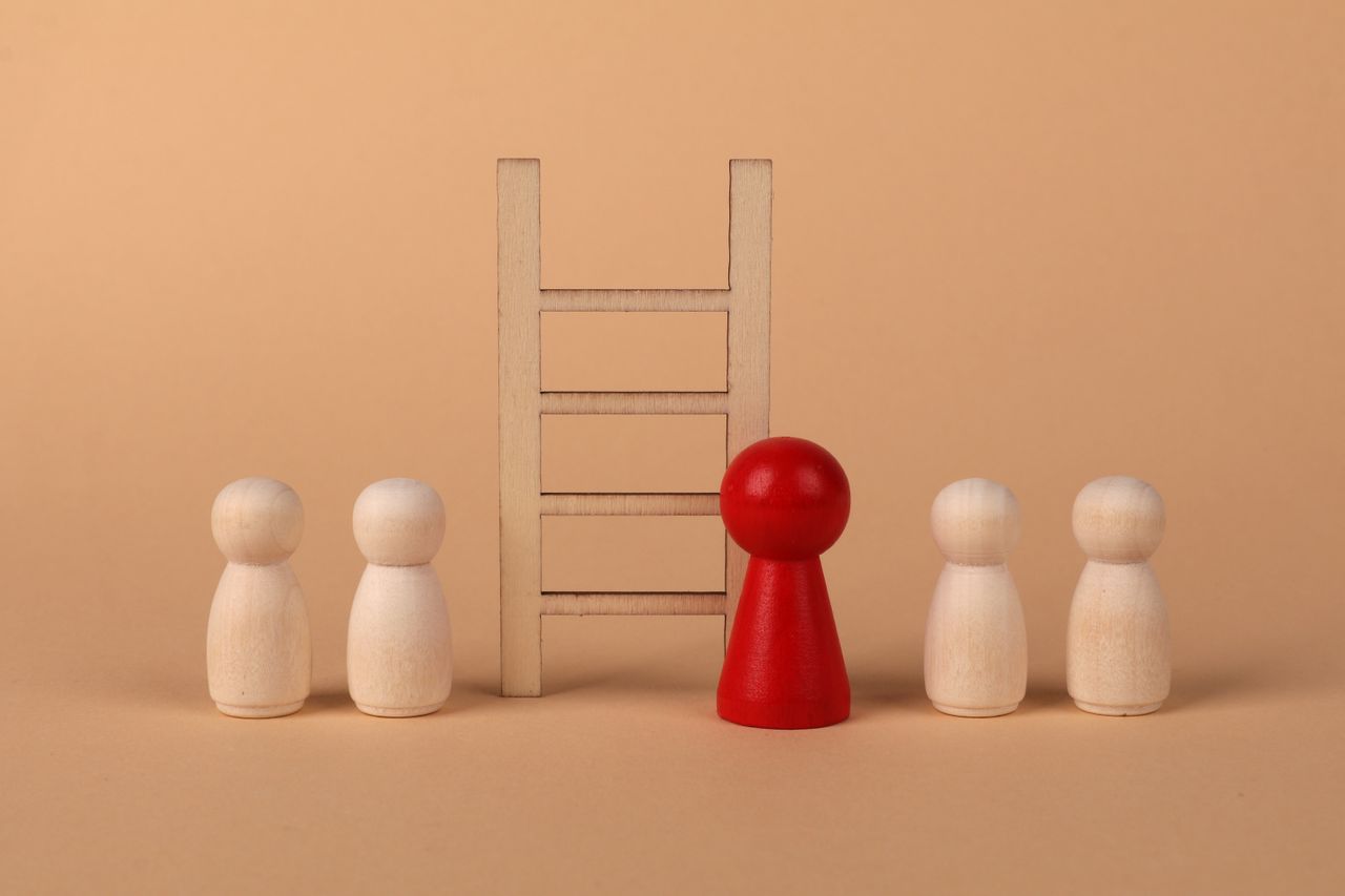 Abstract representation of leadership with wooden figures and ladder on a neutral background.
